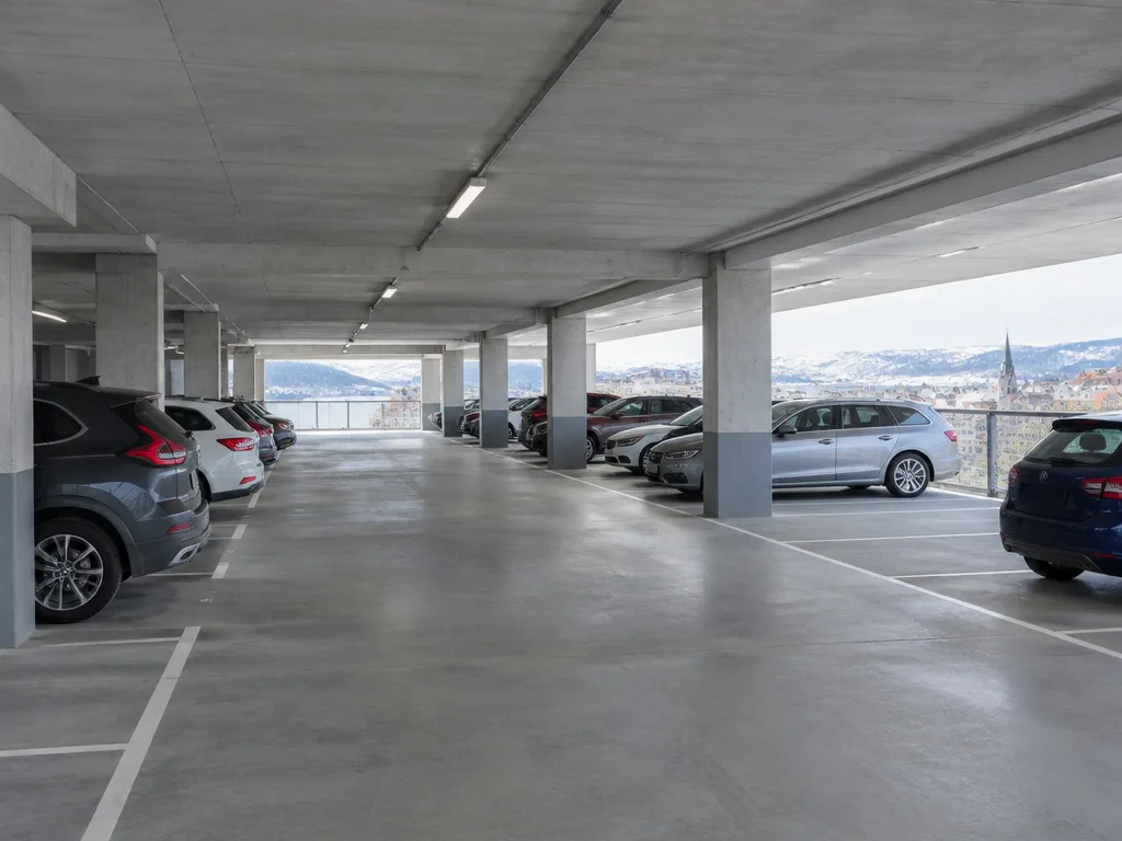 Parkerade bilar mellan betongpelare i ett parkeringshus med utsikt över en stad